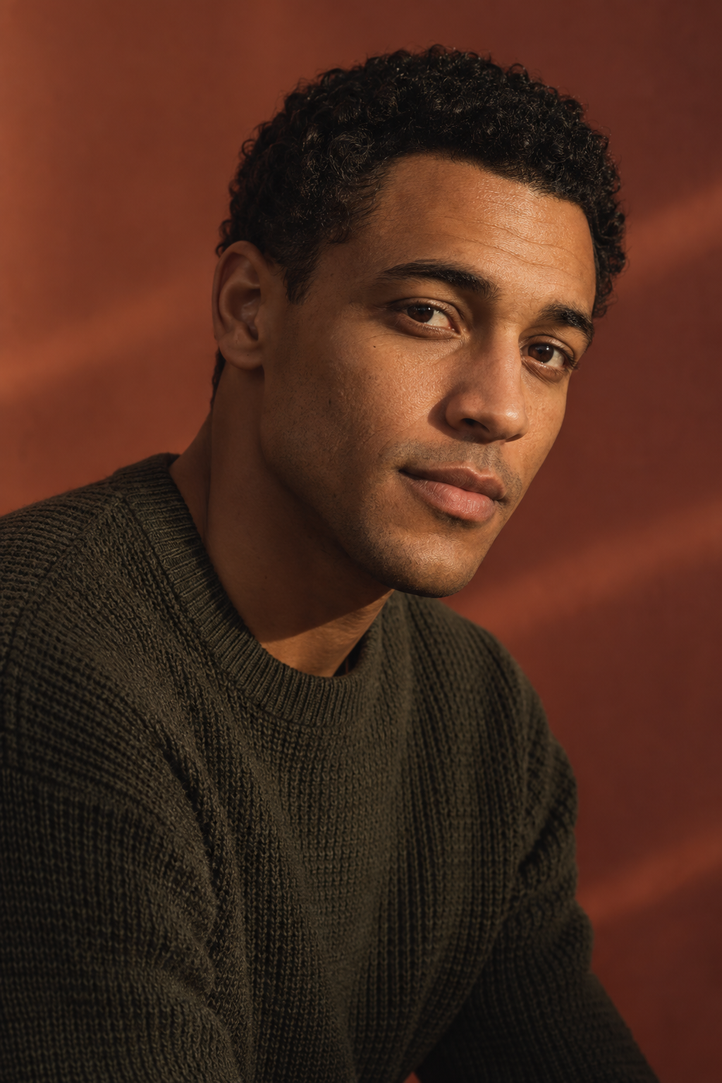 Theo Laurent editorial portrait, short dark curls and olive knitwear